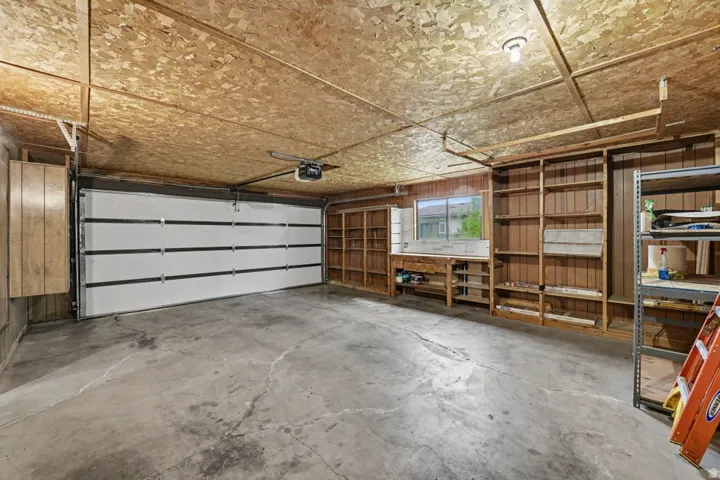 Spacious garage featuring a sectional overhead door, concrete flooring, overhead lighting, integrated shelving, and a built-in workbench with window