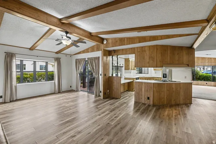 Spacious living area featuring wood-finish flooring, exposed ceiling beams, and an angled ceiling