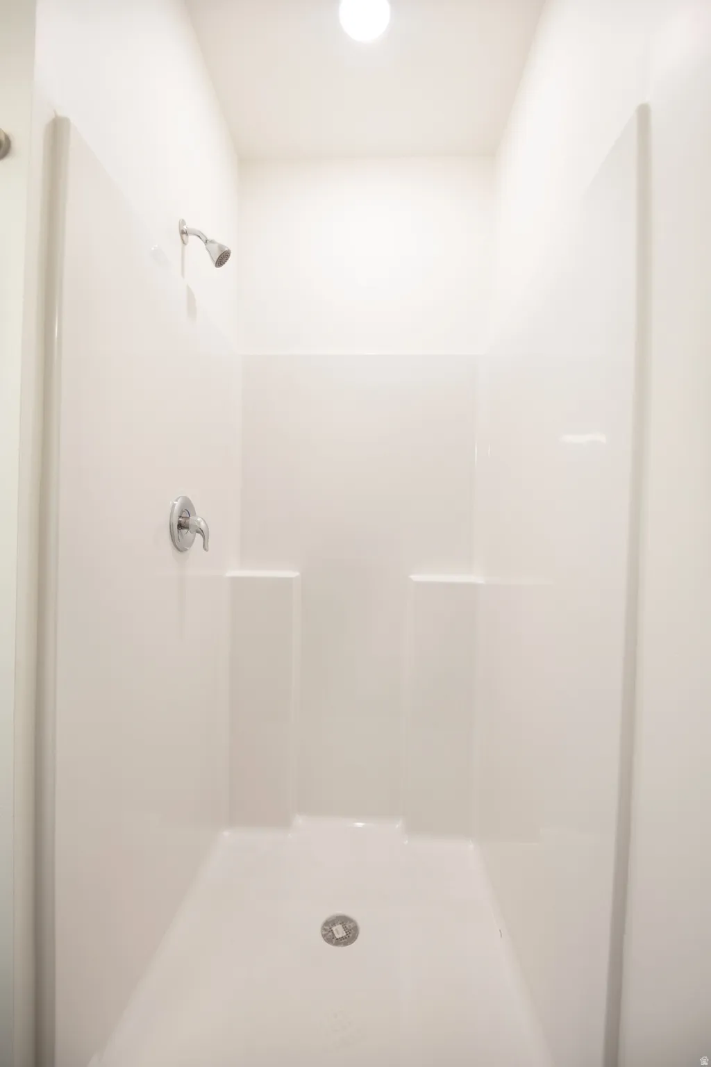 White shower stall featuring a chrome shower head and control handle
