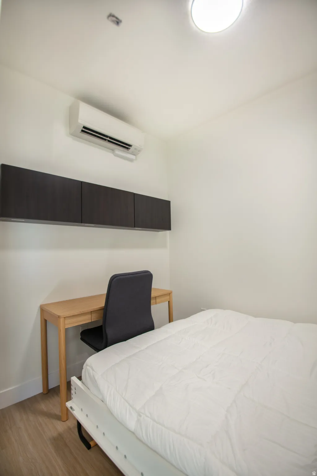 Room featuring wood-finish flooring, white walls, and a built-in wall-mounted air conditioning unit