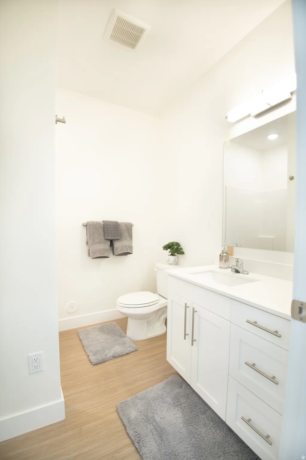 Modern bathroom featuring a white vanity with brushed nickel hardware, a white sink, and light wood-finish flooring