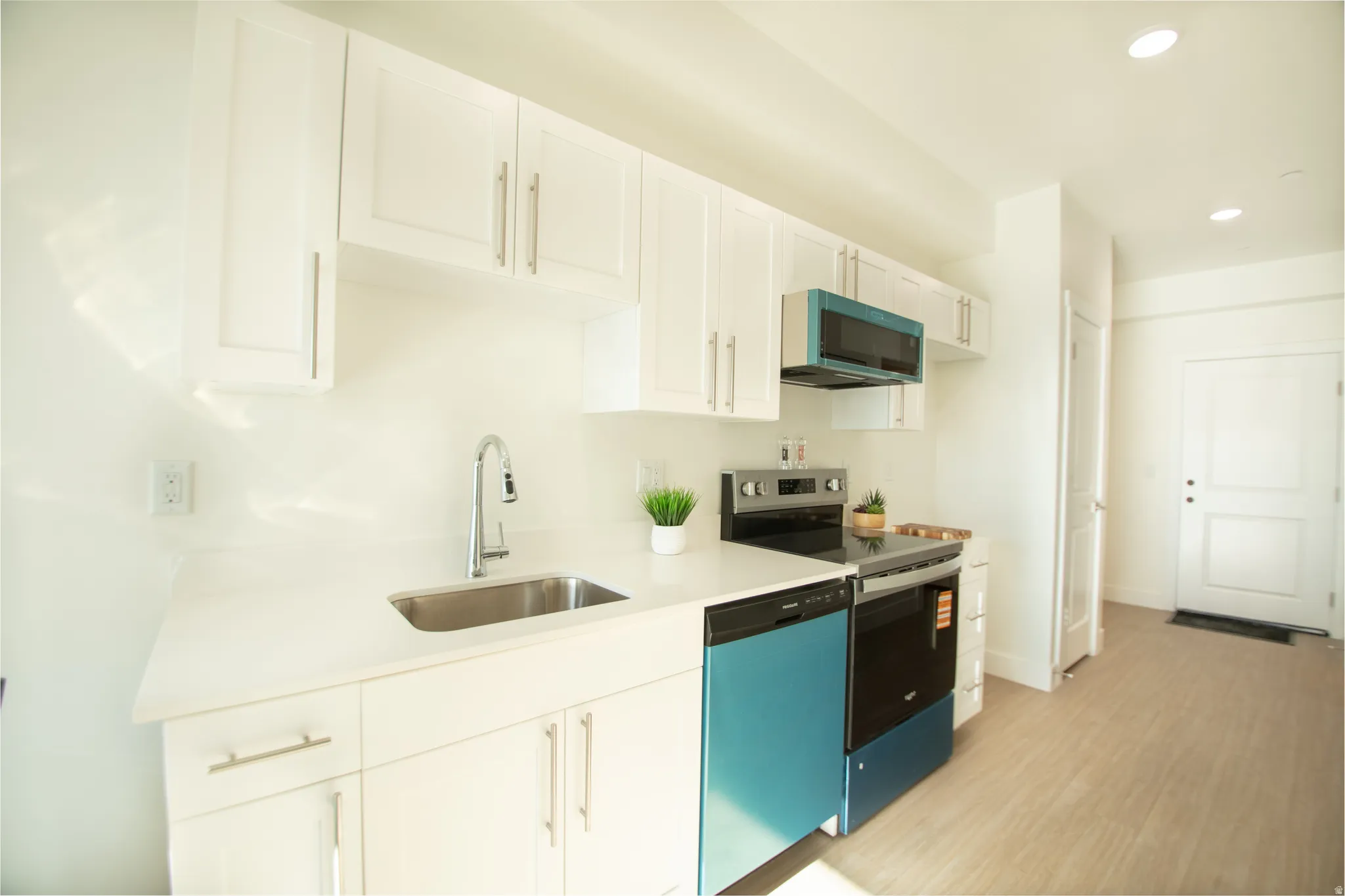 Modern kitchen featuring white cabinetry, light-toned countertops, a stainless steel sink with a gooseneck faucet, and integrated appliances including a range and dishwasher