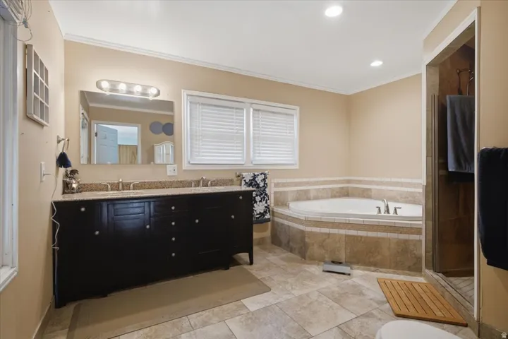 Bathroom featuring a dark wood double vanity with a speckled countertop, a large mirror, and a built-in corner soaking tub with tile surround