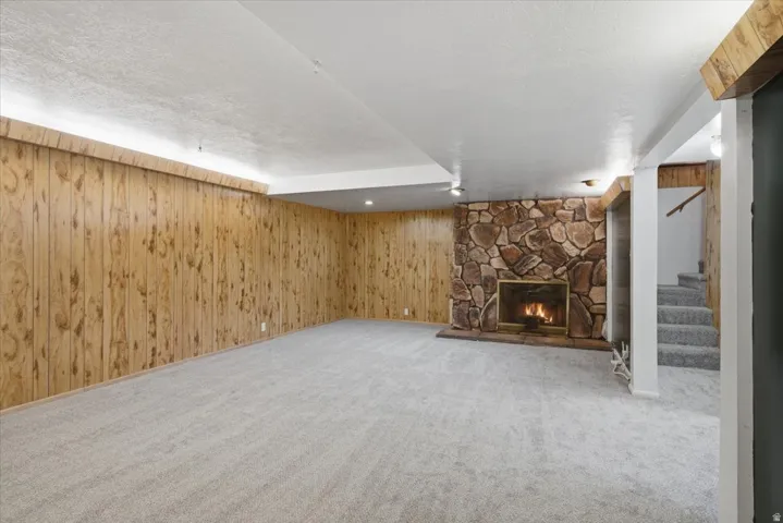 Spacious room featuring wood paneling, a stone-clad fireplace, light-toned carpeting, and recessed lighting