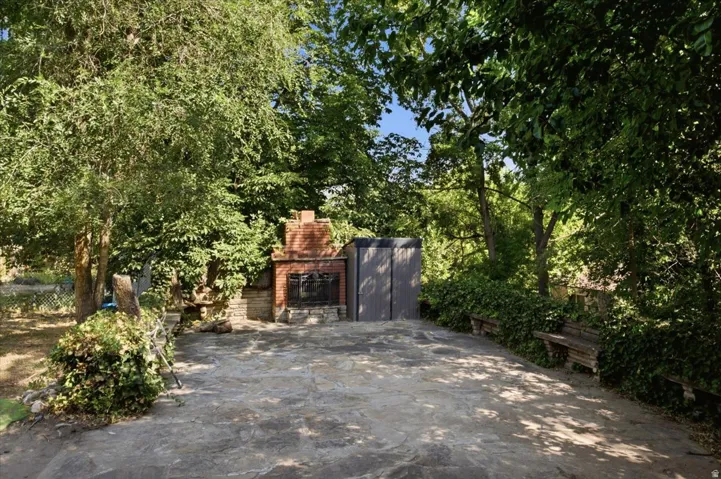 Outdoor patio featuring flagstone paving, a brick fireplace with a stone base, and established shade trees