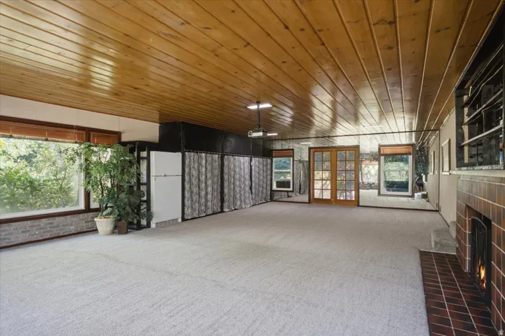 Spacious room featuring wood plank ceiling, light-colored carpet, and a brick-clad fireplace with a metal grate