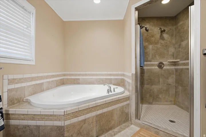 Corner soaking tub with tile surround, adjacent to a glass-enclosed shower featuring tiled walls and floor