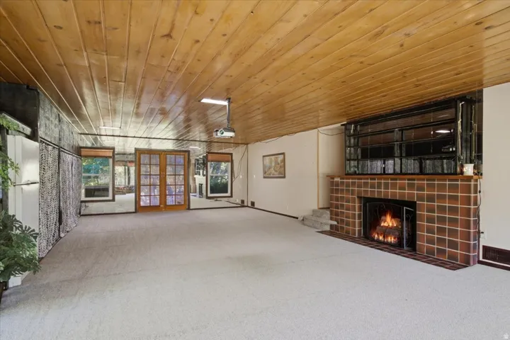 Spacious room featuring a wood-panel ceiling, light-colored carpet, and a brick-tiled fireplace with hearth