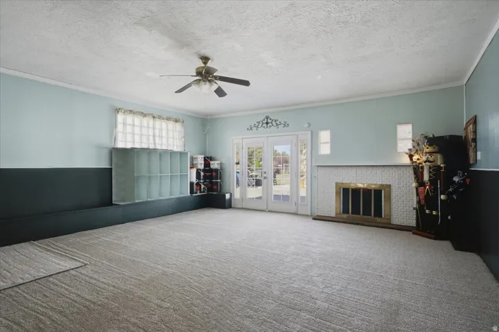 Carpeted interior space featuring a ceiling fan, a fireplace with a white tile surround, and French doors