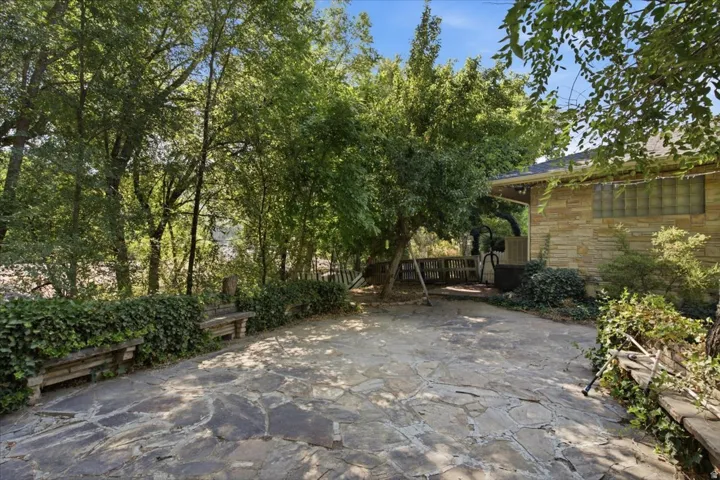 Charming courtyard featuring a rustic stone-paved surface, mature trees providing natural shade, and lush green landscaping