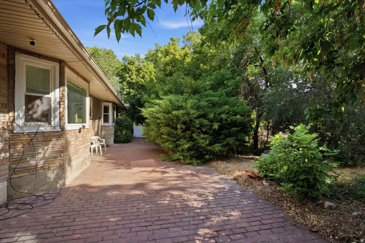 Brick paver pathway with mature landscaping and a stone veneer exterior