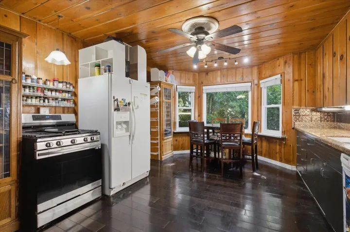 Kitchen featuring wood paneling, dark wood-finish flooring, a white side-by-side refrigerator, and a stainless steel and black range