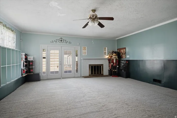 Spacious open floor plan showcasing neutral carpet flooring, ceiling fan with light fixture, and French doors with transom windows flooding the space with natural light
