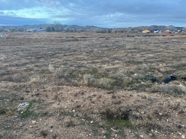 Expansive undeveloped land parcel featuring natural grasses and distant residential structures