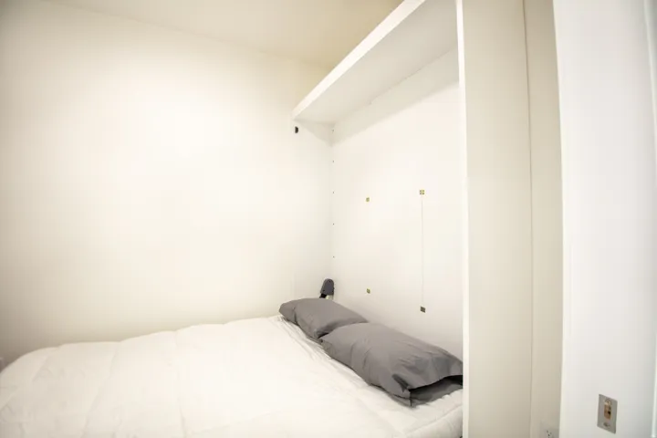 Integrated wall unit with a built-in bed platform, white shelving, and a white wall-mounted upper cabinet