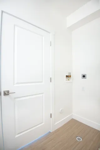Utility area featuring panel door with brushed nickel hardware, light wood-finish flooring, white baseboards, and bright white walls