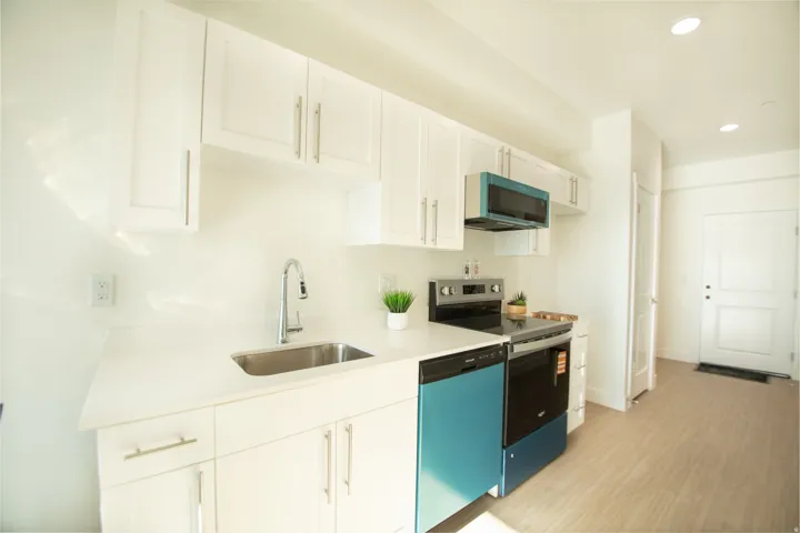 Modern kitchen featuring white cabinetry, light-toned countertops, a stainless steel sink with a gooseneck faucet, and integrated appliances including a range and dishwasher