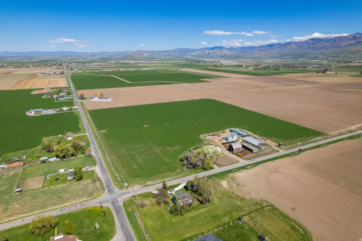 Expansive agricultural land featuring a farmstead with multiple outbuildings, cultivated fields, and paved road frontage