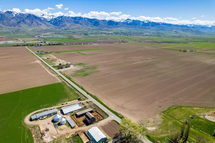 Expansive agricultural property featuring productive irrigated farmland, established outbuildings with equipment storage, paved farm road access, and panoramic mountain backdrop