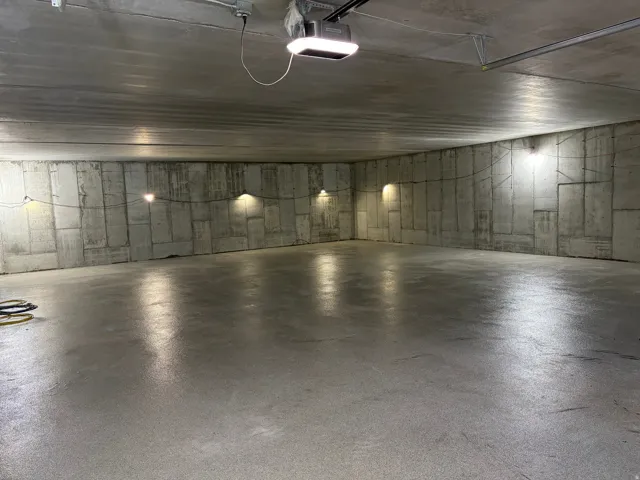 Spacious concrete garage with exposed concrete walls, polished concrete flooring, and multiple wall-mounted light fixtures