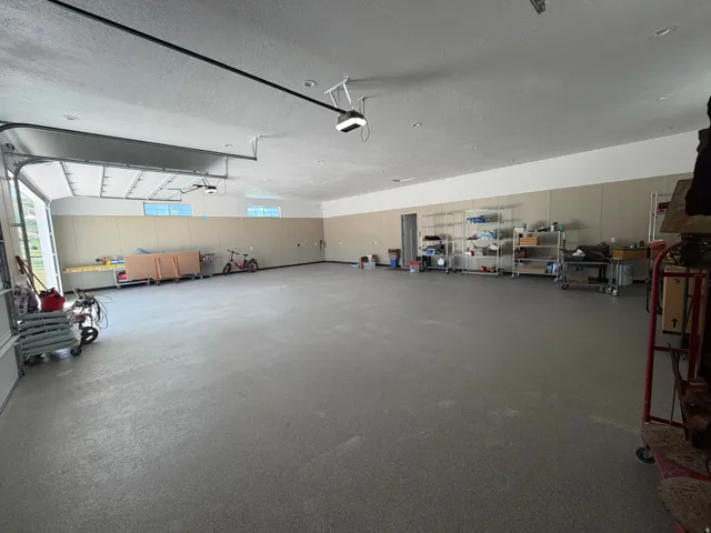Expansive garage space with a large overhead door, textured concrete flooring, and an abundance of natural light from multiple windows