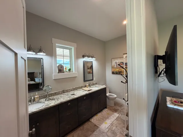 Spacious bathroom featuring a double vanity with granite-style countertops, dark wood cabinetry, and a window for natural light