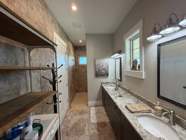 Bathroom featuring dual vanity with granite countertop and undermount sinks, hexagonal floor tiles, and a tiled shower with a small window