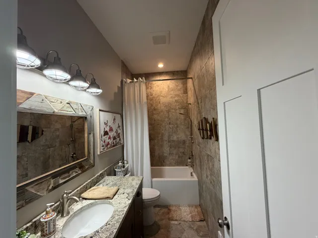 Bathroom featuring a full-sized bathtub with shower, tiled walls, and a single vanity with stone countertop