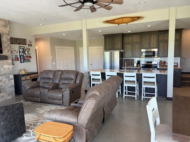 Open-concept living space featuring a gourmet kitchen, stone accent wall, recessed lighting, wood-finish ceiling fan, and durable flooring