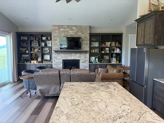 Open-concept living space featuring a stone-clad fireplace with a wood mantel, built-in cabinetry, wood-finish flooring, and a sliding glass door