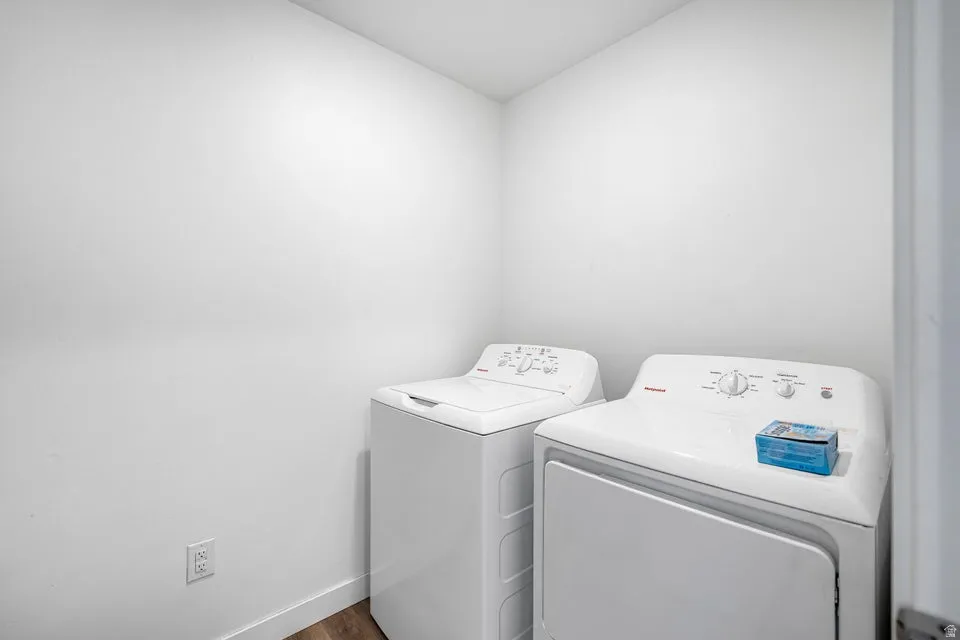 Laundry area featuring a top-load washing machine, front-load dryer, and wood-finish flooring