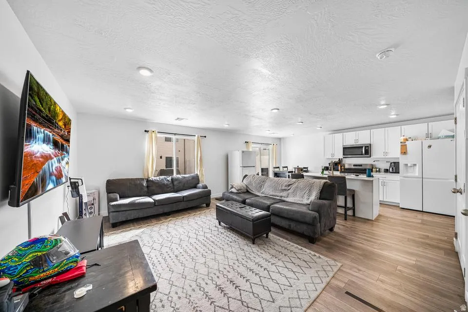 Spacious open-concept living area featuring recessed ceiling lighting, wood-finish flooring throughout, and a neutral color palette