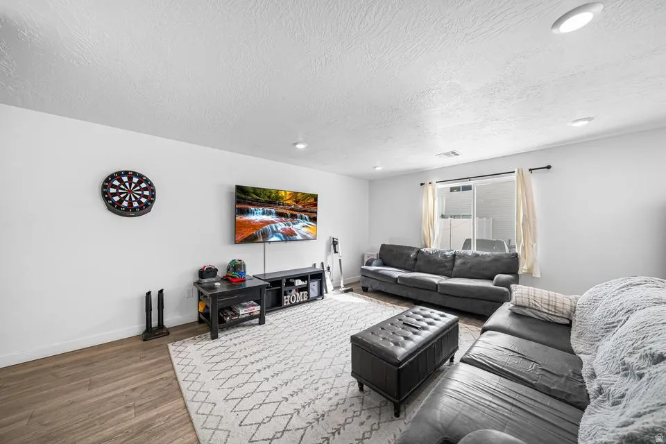 Spacious recreational room featuring wood-finish flooring, recessed ceiling lighting, and large windows with natural light
