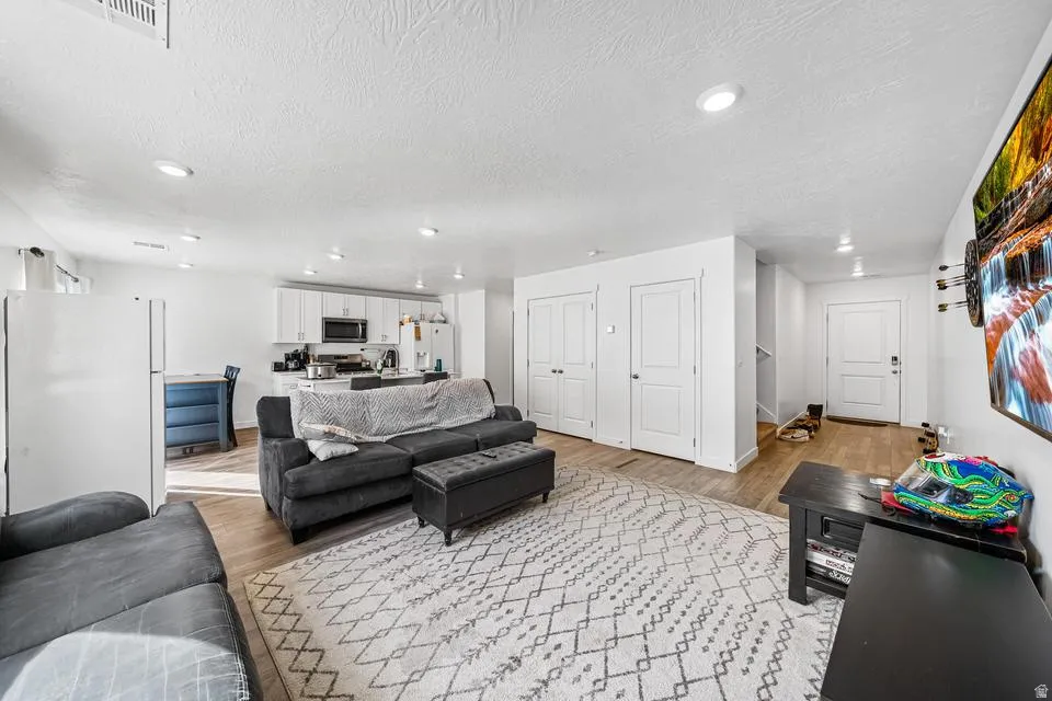 Spacious finished basement featuring a black leather sectional sofa, geometric patterned area rug, wood-finish flooring, and recessed ceiling lighting