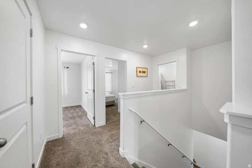 Bright upper-level hallway featuring recessed lighting, pristine white painted walls, and neutral carpet flooring