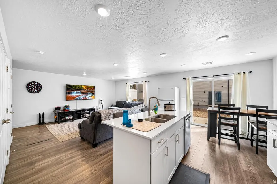 Open-concept living space featuring wood-finish flooring, recessed lighting, and a kitchen island with an undermount double-basin stainless steel sink