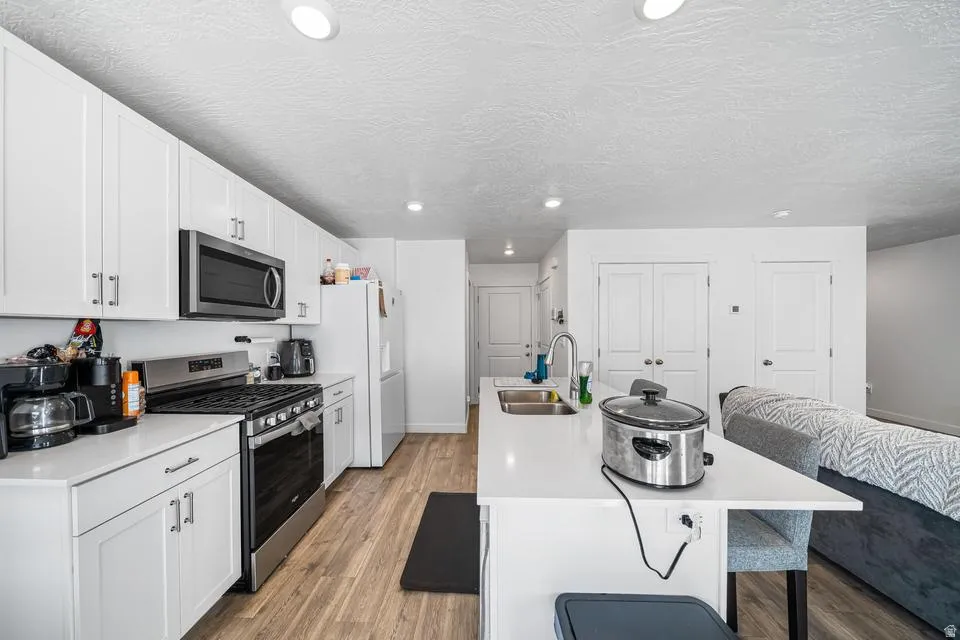 Modern kitchen and living space featuring white cabinetry with stainless steel appliances, including a gas range and microwave