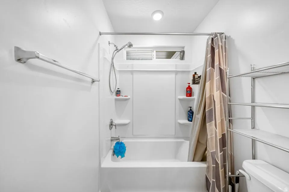 Tub and shower combination featuring a built-in shelf and an overhead window with horizontal blinds