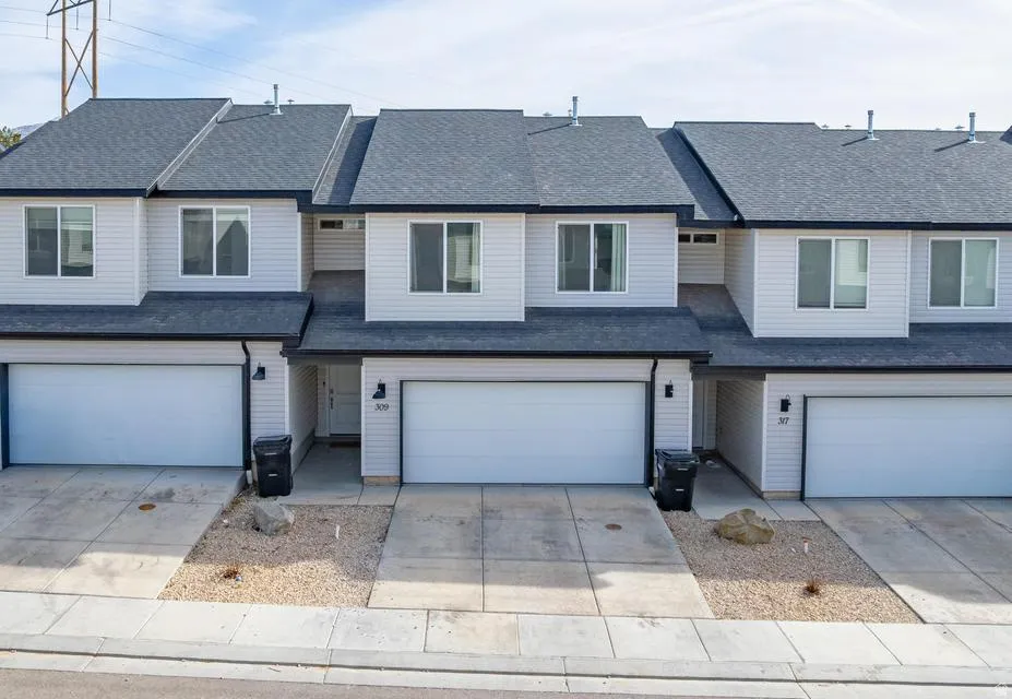 Contemporary townhome exterior featuring light-colored siding, dark shingle roofing, and integrated single-car garages