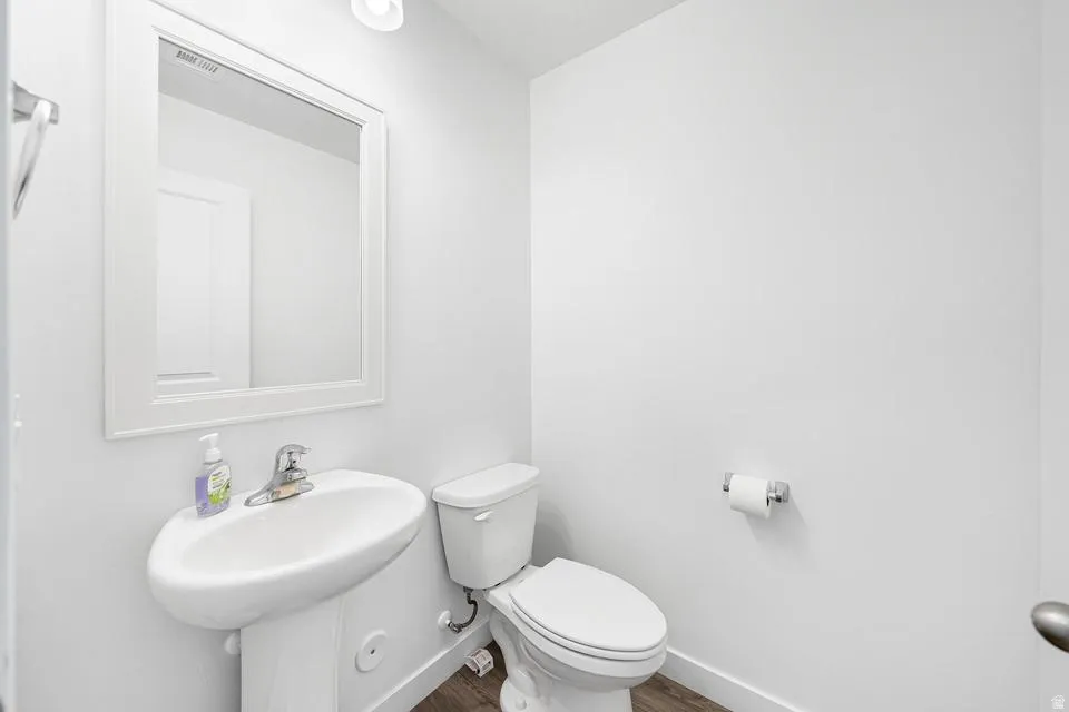 Compact powder room featuring a white pedestal sink, white framed mirror, and wood-finish flooring