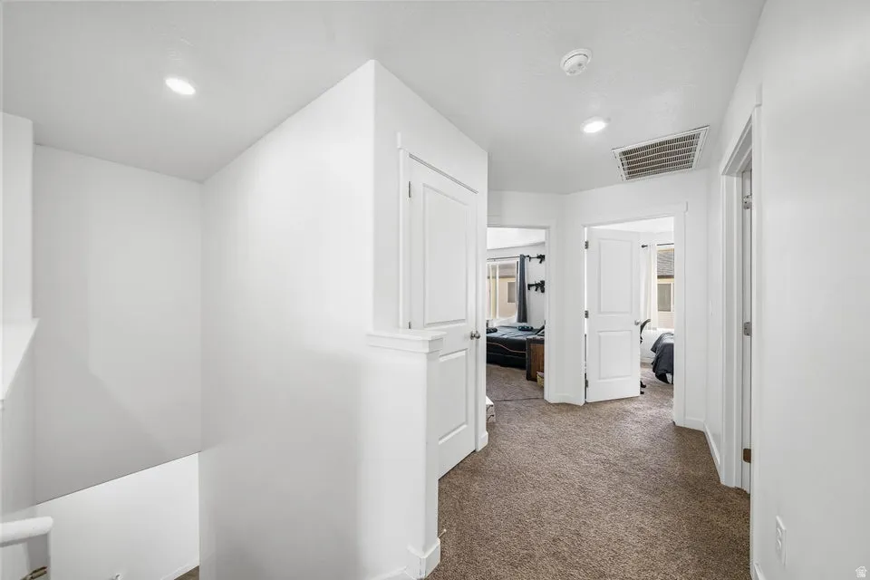 Upper-level hallway with neutral carpet flooring and recessed lighting