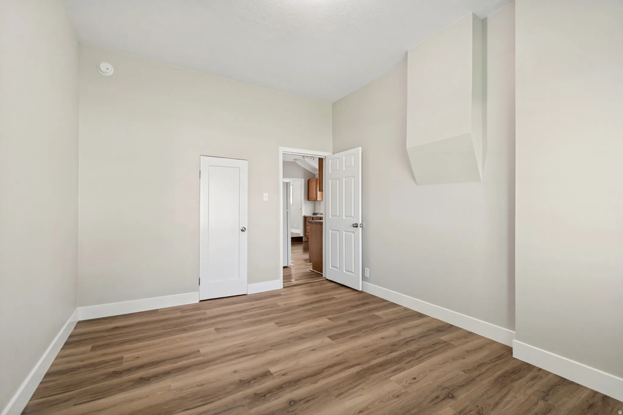 Spacious room featuring wood-finish flooring, light neutral wall paint, and white baseboards