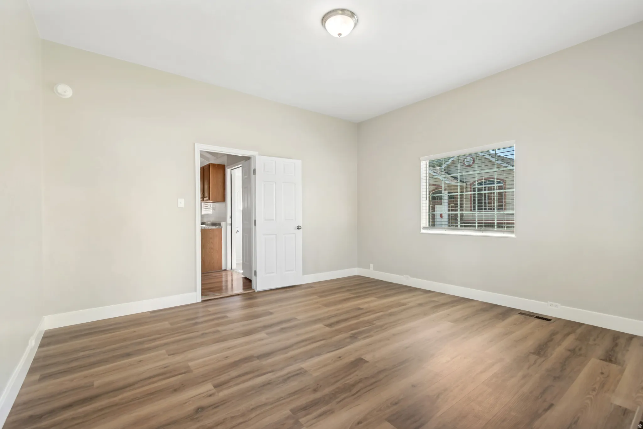 Spacious bedroom featuring hardwood-finish flooring, neutral wall finishes, and abundant natural light from a large window