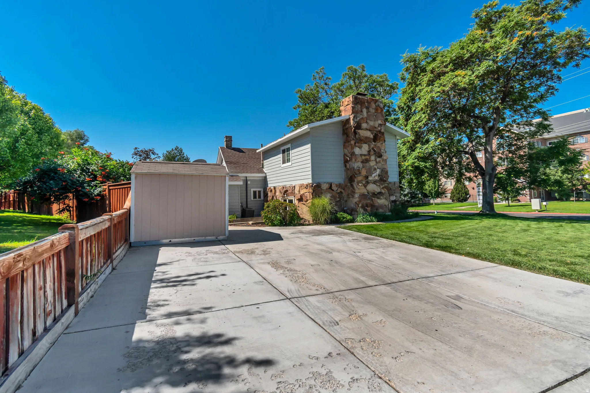 Spacious driveway and entry featuring a wide concrete approach, attached garage with neutral-toned exterior, and distinctive stone chimney