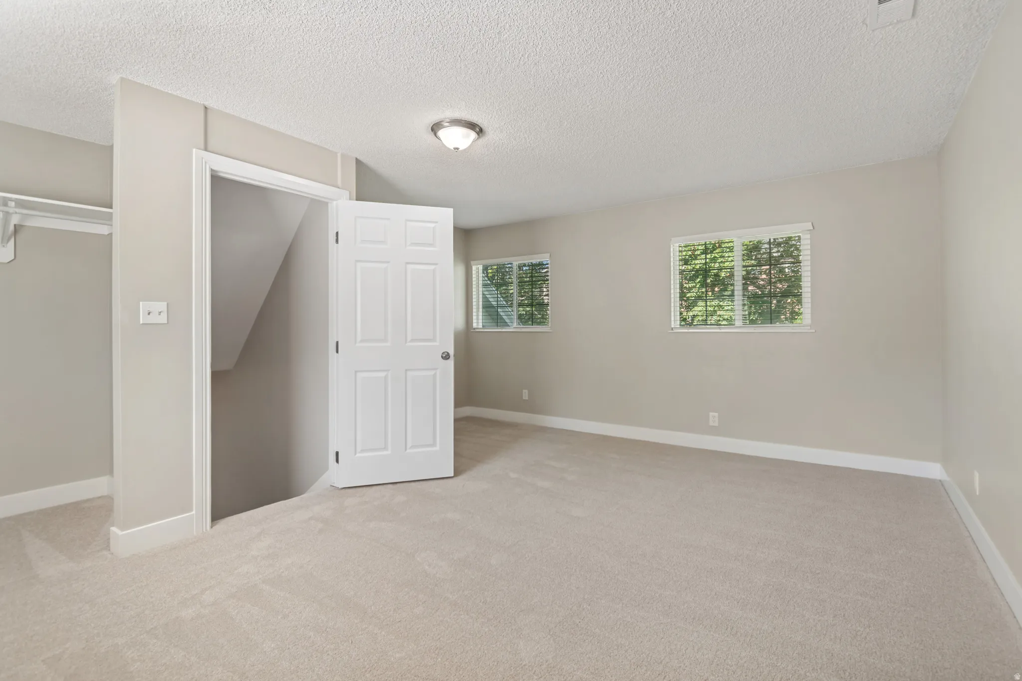 Carpeted room featuring two windows, an open doorway, and a built-in closet with shelving and hanging rod