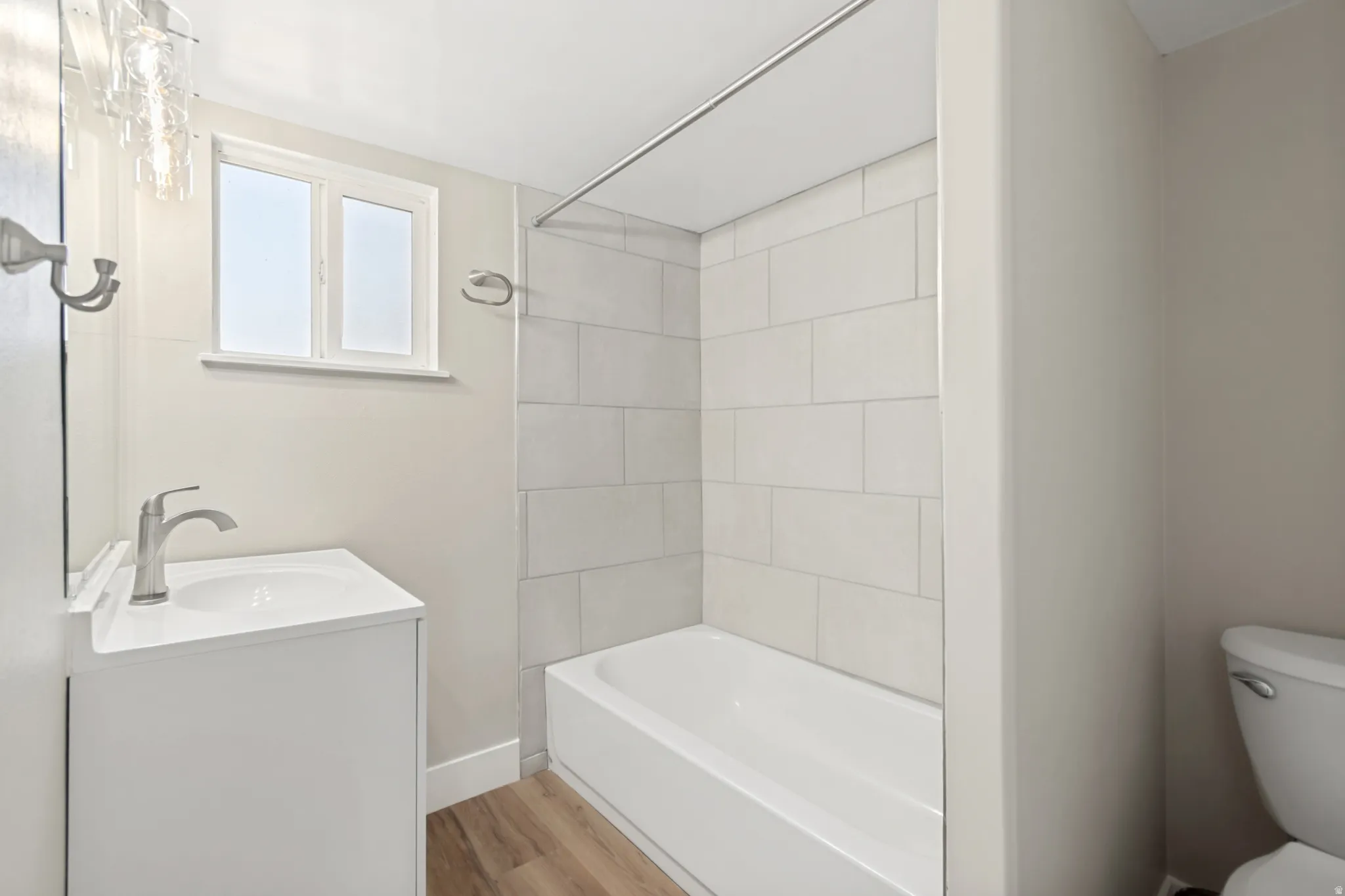 Bathroom featuring a white vanity with integrated sink, brushed nickel faucet, a window, and a bathtub with subway tile surround