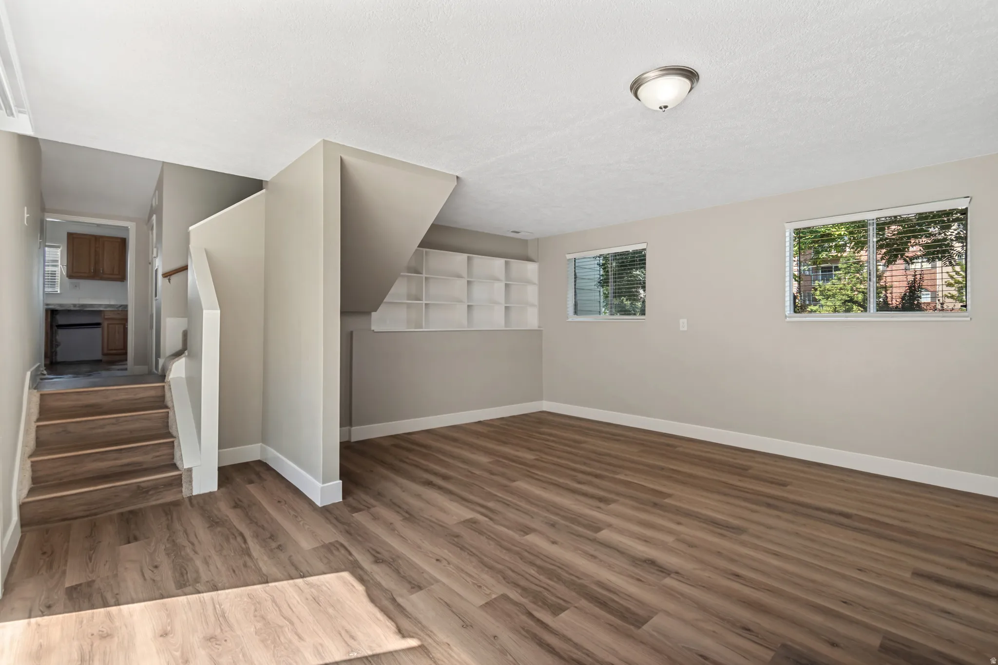Spacious main room showcasing wood-finish flooring, neutral wall finishes, and abundant natural light from multiple windows