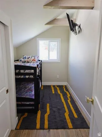 Attic space featuring a white-framed window, wood-finish flooring, and sloped ceilings with exposed beams
