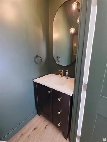 Powder room featuring a dark wood vanity with a white countertop and integrated sink, gold-tone faucet, oval wall mirror, and wood-finish flooring