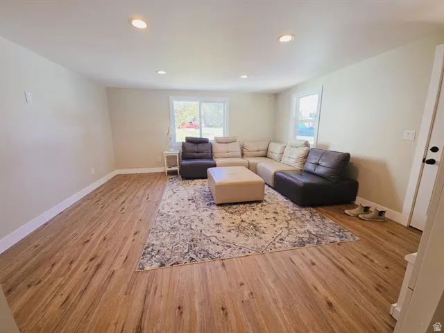 Spacious recreation room featuring gleaming wood-finish flooring, recessed ceiling lighting, and abundant natural light from multiple windows